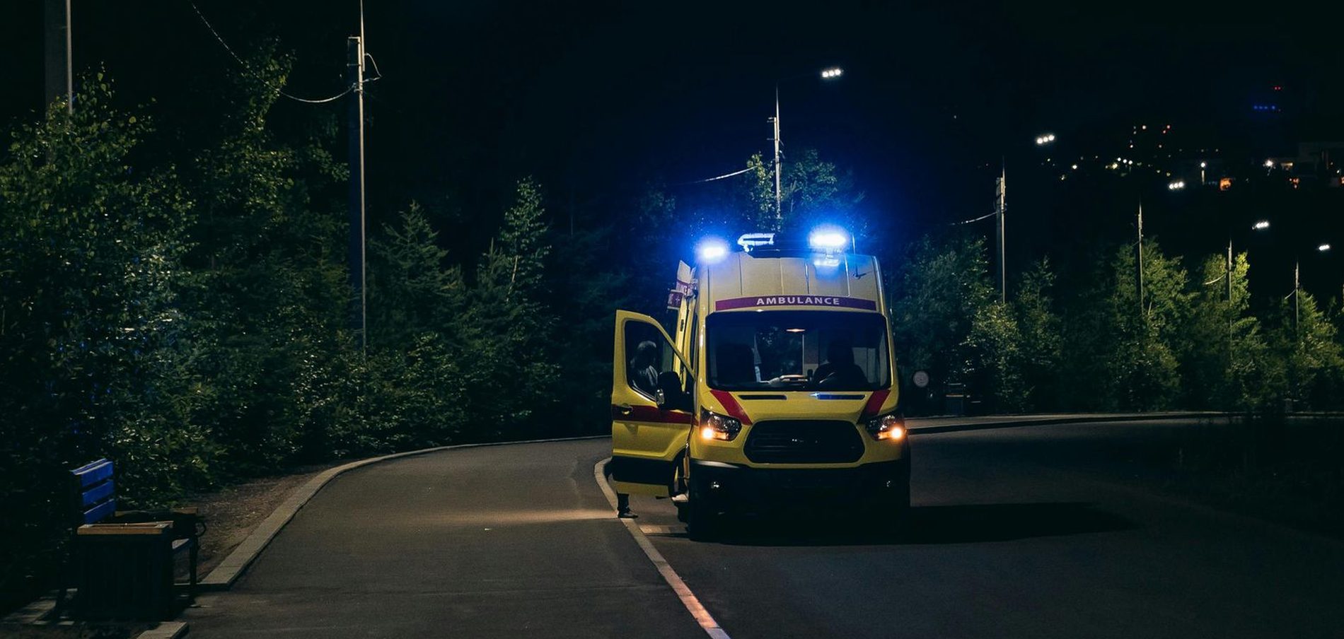 An ambulance stopped on a road at night with its lights on