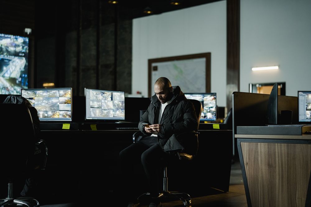 An operator watching a wall of monitoring screens in a dark control room